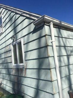 Side of a house with light blue siding, white window and gutter against a bright blue sky.