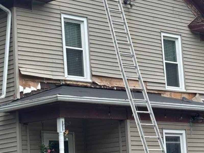 Ladder propped against house siding with exposed damage near the roofline.