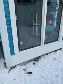 Blue and white building with windows, reflected garden, and snow on the ground.