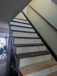 Staircase with wooden steps and a dark railing, leading upward. Painted white risers and brown treads.