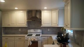 Cream-colored kitchen cabinets with a stainless steel range hood. Granite countertops, recessed lighting.