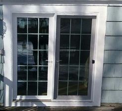 Sliding glass door with white frame and grid pattern, gray screen, installed in light blue siding.