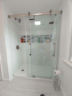 Glass shower with sliding door in a white bathroom. Toilet paper stand is in the lower right.