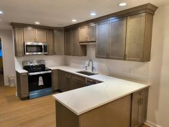 U-shaped kitchen with gray cabinets, white countertops, stainless steel appliances, and white tiled backsplash.