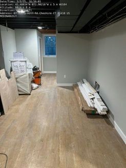 Renovated room interior with light wood-look flooring and gray walls. Window at the end of the hall. Construction materials on the floor.