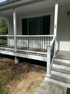 White porch with black railing and steps leading to a house with a sliding glass door.