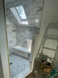 Newly tiled shower with skylight and built-in bench. Hexagon floor tiles and rectangular wall tiles. Ladder on the right.