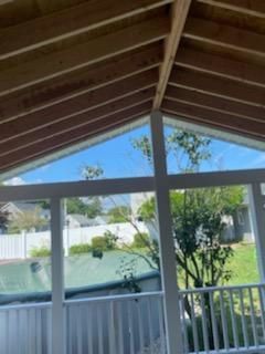 View from a screened porch with white trim, looking out at a yard with a fence and trees, bright blue sky visible.
