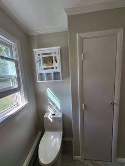 Bathroom with a toilet, cabinet, window, and closed door, all in neutral tones.
