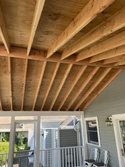 Wooden ceiling with rafters and plywood, visible from below, over a porch.
