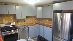 Kitchen renovation in progress, light blue cabinets, stainless steel appliances, exposed wall behind cabinets.