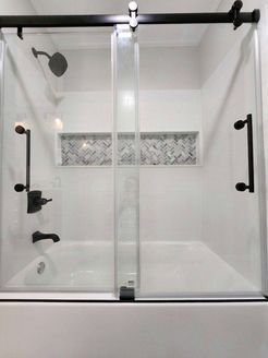 Modern shower stall with sliding glass doors, black hardware, white walls, and decorative tile.