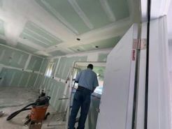Man working on drywall in a room under construction, with a partially open door in the foreground.