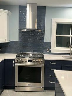 Kitchen with blue cabinets, stainless steel range, and tile backsplash under a vent hood.