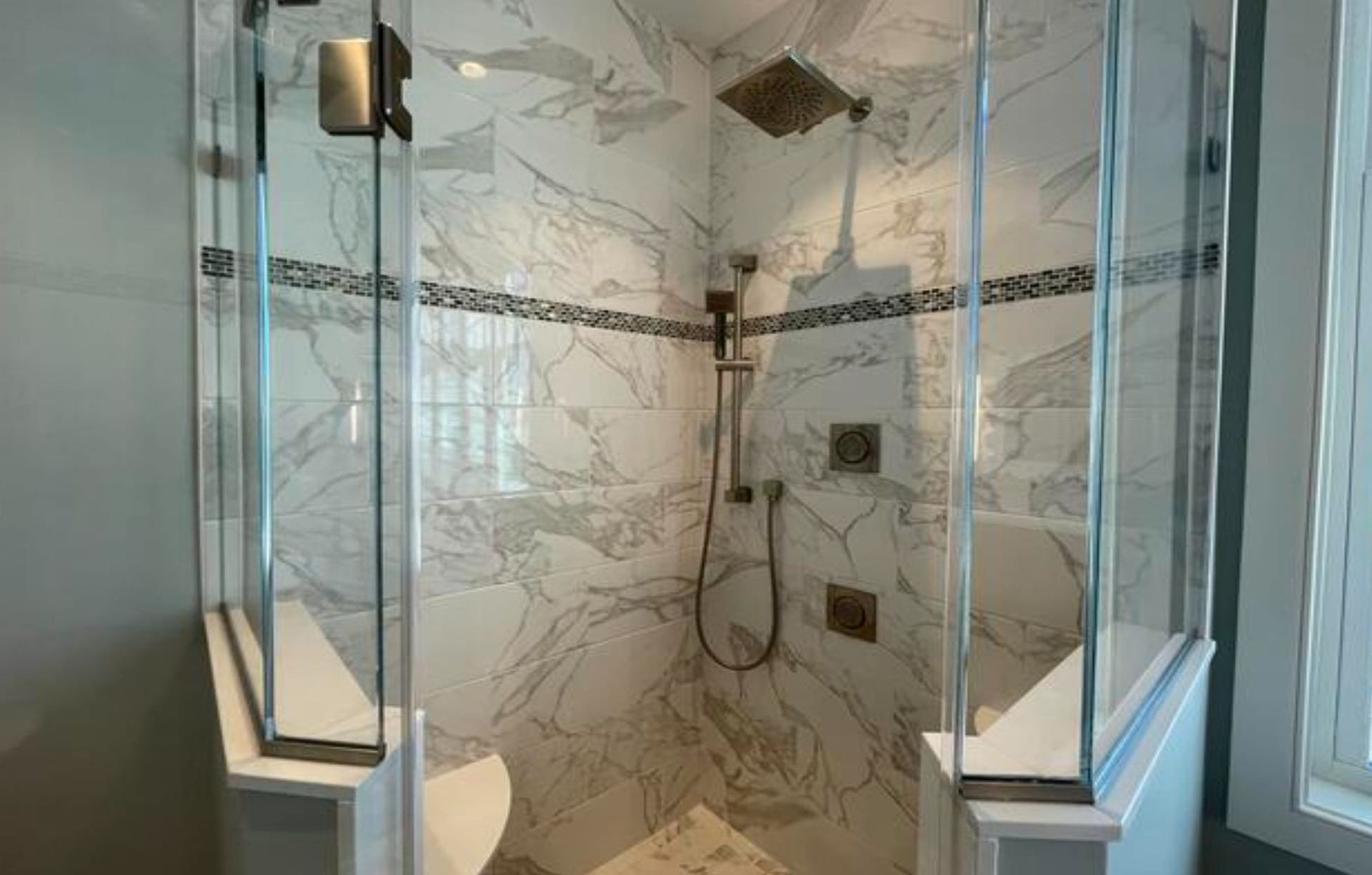 Glass-enclosed shower with white marble walls, a decorative tile stripe, and multiple showerheads.