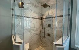 Glass-enclosed shower with white marble walls, a decorative tile stripe, and multiple showerheads.