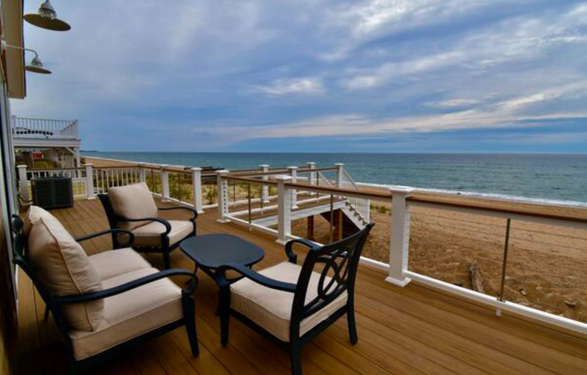 Deck with seating overlooking a beach and ocean under a cloudy sky.