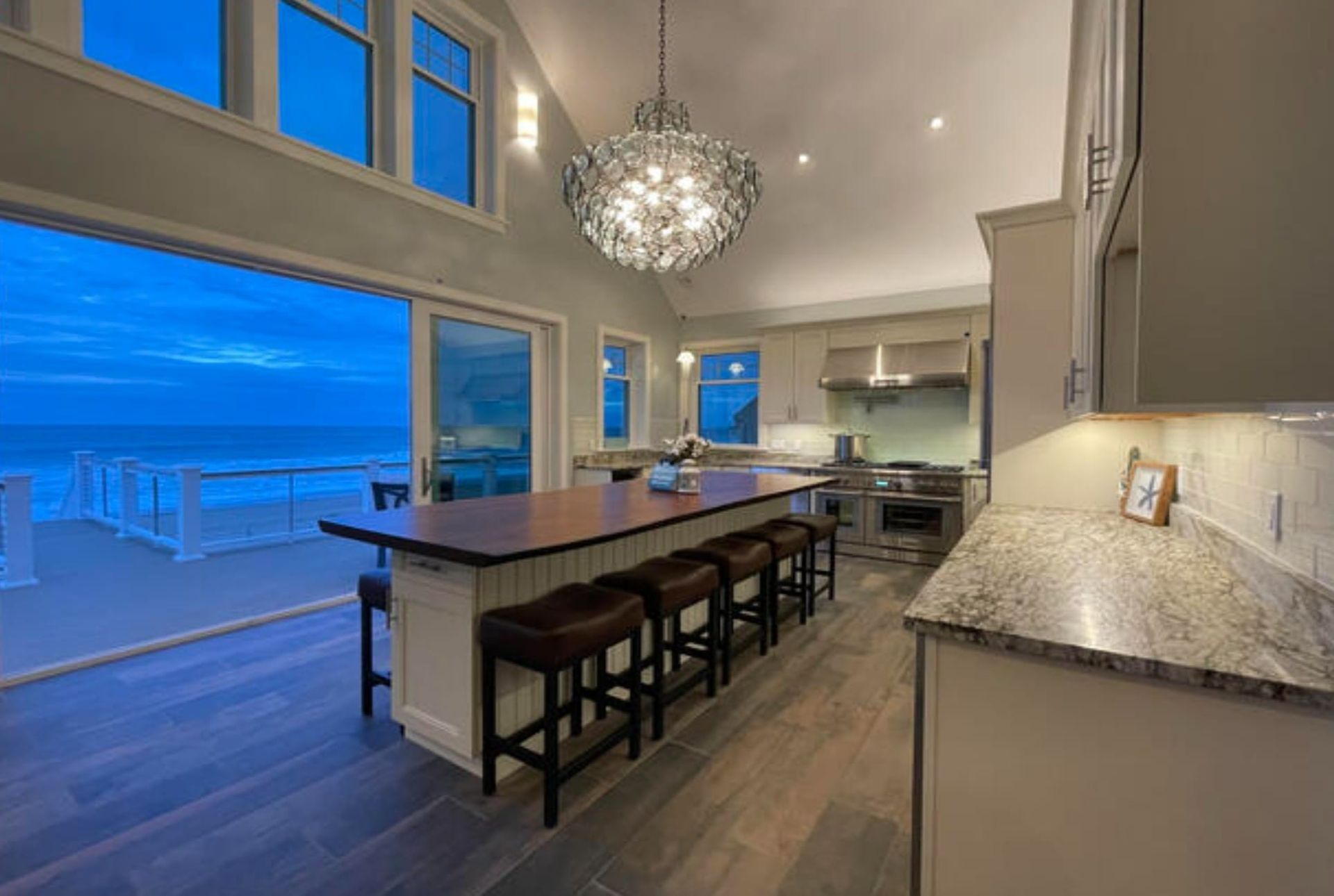 Luxury kitchen with ocean view. Open to a deck, featuring a large island, chandelier, and stainless steel appliances.