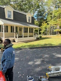 Person in blue jacket standing near house with porch, sunny day.