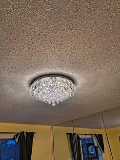 Crystal chandelier on a textured ceiling, illuminating a yellow-walled room with a window and mirror.