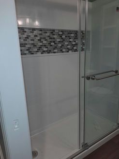 White shower stall with mosaic tile accent and glass door.