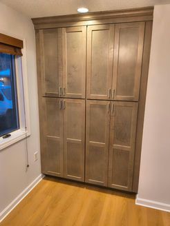 Tall, gray cabinet with eight doors, built into the corner of a room, next to a window.