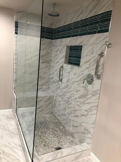 Modern shower with glass doors, marble-look tiles, mosaic tile accent, built-in bench, and rain showerhead.