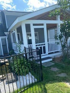 Screened porch addition on a gray house with white trim. Black fence in foreground, grass and small garden.