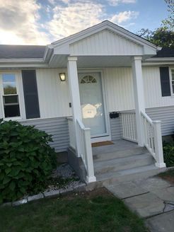 White house with a small porch, steps, and front door. Light blue siding with black shutters.
