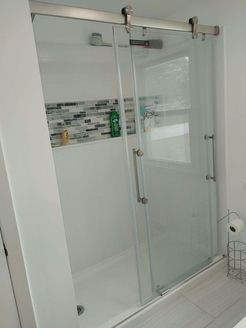 Glass sliding shower door with chrome hardware, white walls, and a mosaic tile accent.