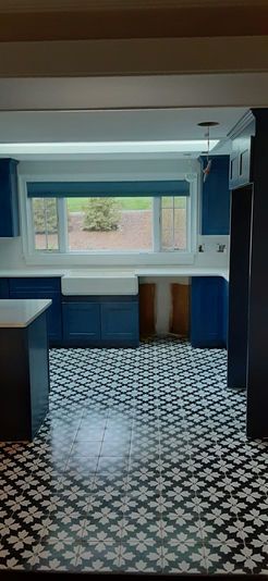 Kitchen with blue cabinets, white countertops, patterned tile flooring, and a large window with a shade.