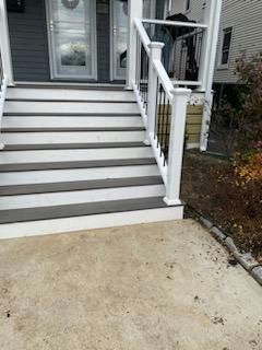 Gray and white deck stairs leading to a front door with a white railing. Concrete path in front.