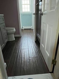 Bathroom with dark brown wood-look tile flooring, white door, and pale purple and blue walls.