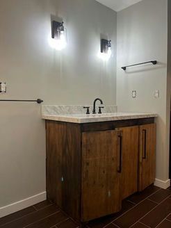 Bathroom with wooden vanity, marble countertop, black fixtures, and sconce lighting.