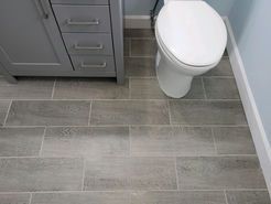 Gray wood-look tile floor in a bathroom, with a gray cabinet and a white toilet.