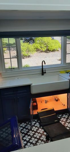 Kitchen sink with a window overlooking a green yard and black faucet. Navy blue cabinets and patterned floor.