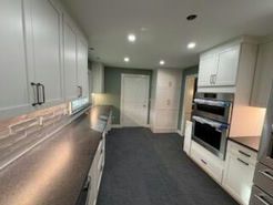 Modern kitchen with white cabinets, dark countertops, stainless steel appliances, and a gray carpeted floor.