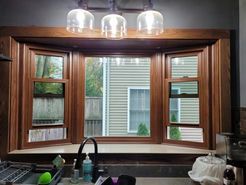 Bay window with wood frame and three hanging lights above a kitchen sink.