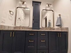 Bathroom with navy blue vanity, two mirrors, and a tall cabinet.