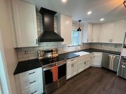 Modern kitchen with white cabinets, dark countertops, and stainless steel appliances.