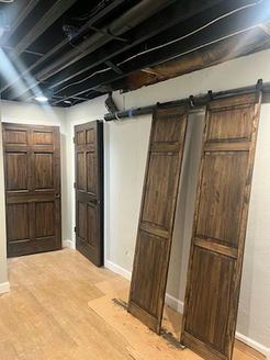 Wooden barn doors and a traditional door in a room with light wood floors and white walls.