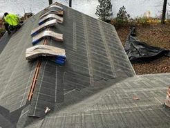 Roof being shingled; worker on roof, shingles and underlayment visible.
