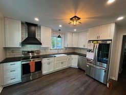 White kitchen with dark countertops, stainless steel appliances, and dark hardwood floors.