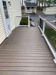 Wooden deck with railing, leading to a yard with sheds.