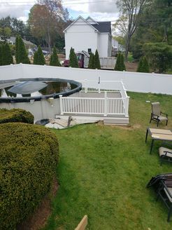 Backyard with above-ground pool, white deck, green lawn, white fence, and a white house in the background.
