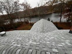 Gray shingled roof with a rounded dome section, overlooking a lake and trees.