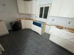 Kitchen under construction; white cabinets, blue sink, dark tile floor, window.
