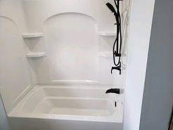 White alcove bathtub with black shower fixtures and two built-in shelves.