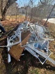 Pile of discarded windows and frames on the ground outdoors, near a road.