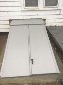 Closed gray bulkhead doors leading to a basement on a building's exterior.